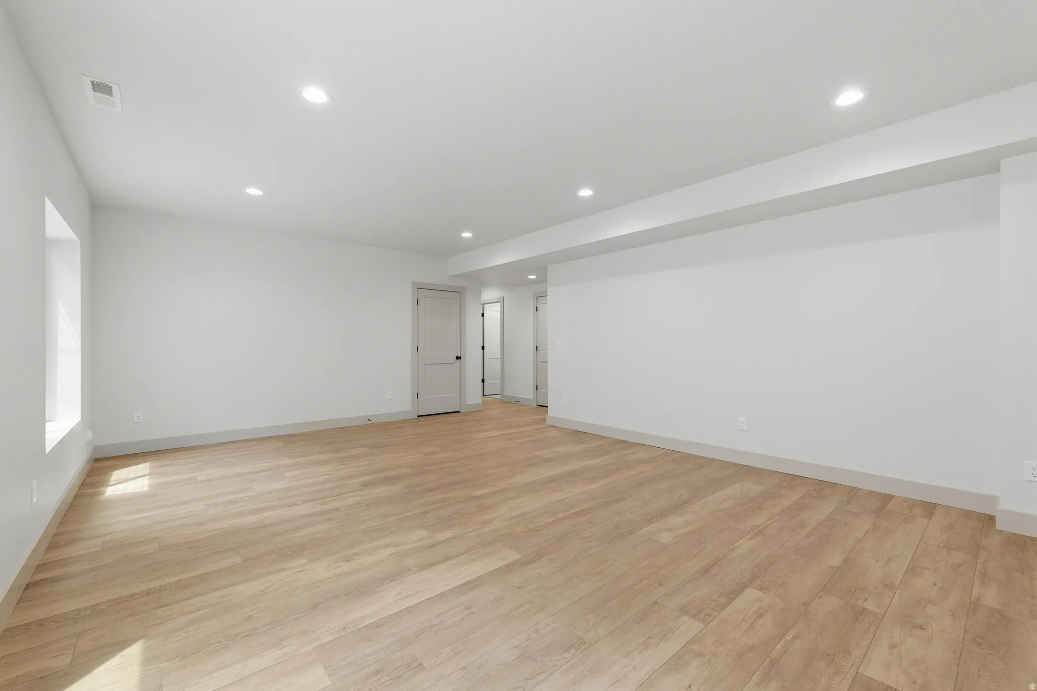 Spacious room featuring light wood-finish flooring, recessed lighting, and a neutral color palette