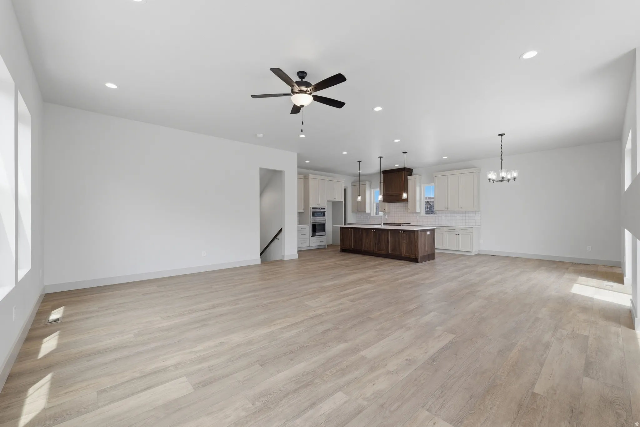 Spacious open-concept area featuring light wood-finish flooring, recessed lighting, and a modern ceiling fan