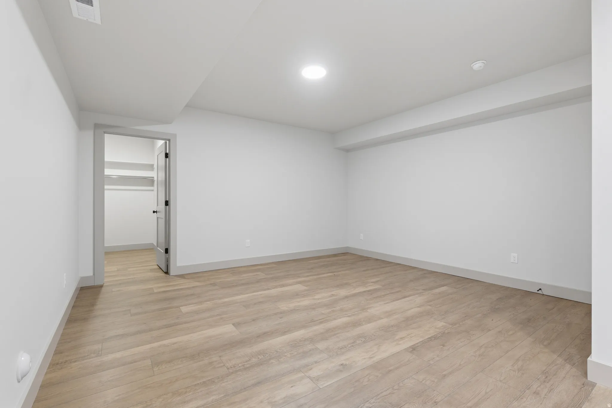 Spacious room featuring wood-finish flooring, white walls, and a recessed ceiling light