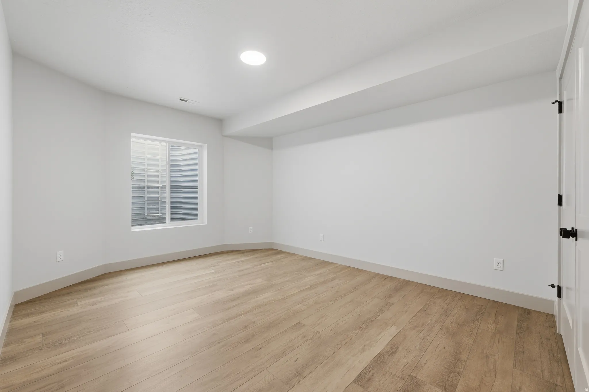 Spacious room featuring wood-finish flooring, recessed lighting, a window with a window well, and crisp white walls