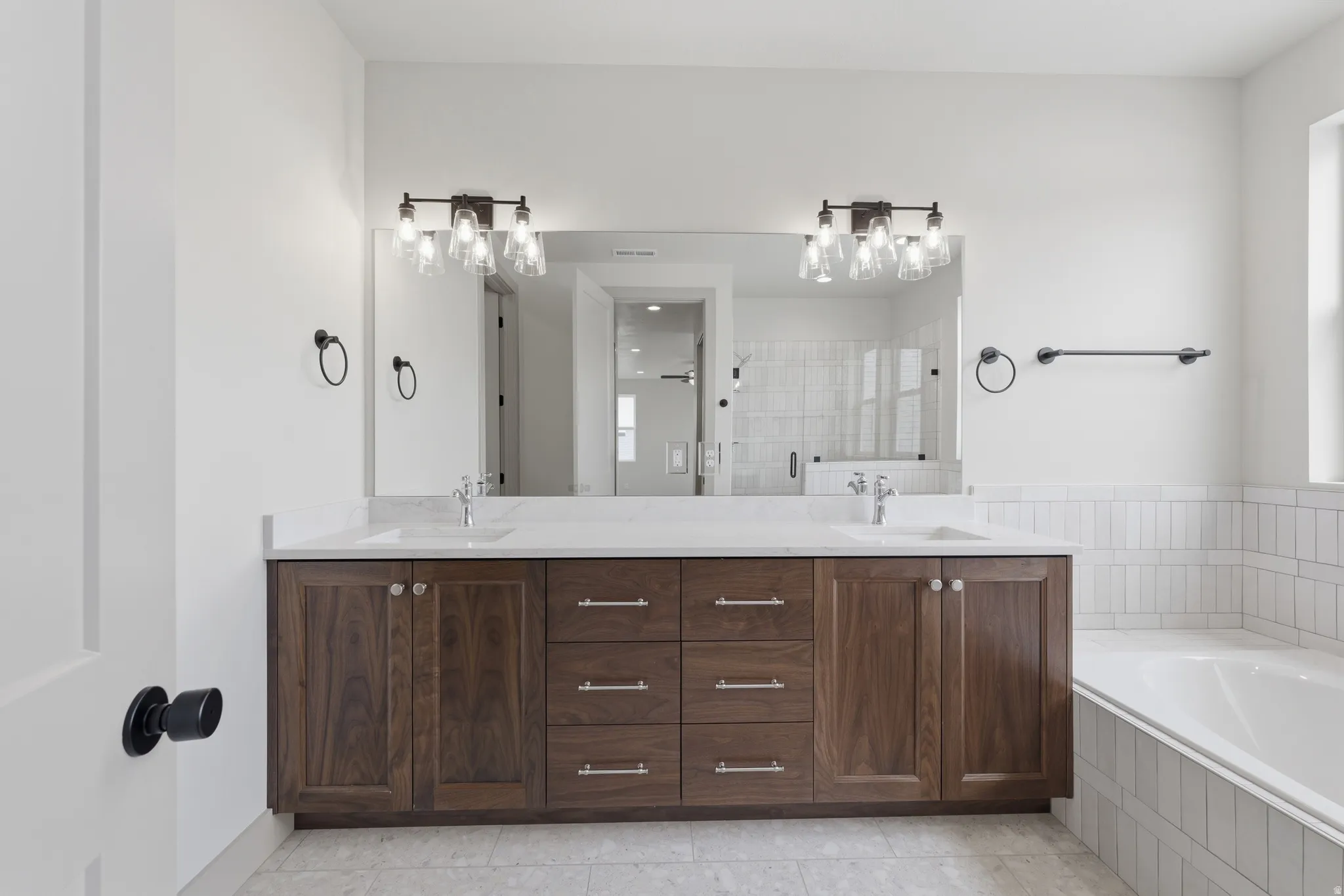 Primary Bathroom. Double vanity with wood-finish cabinetry, white stone countertops, dual undermount sinks, and contemporary lighting fixtures