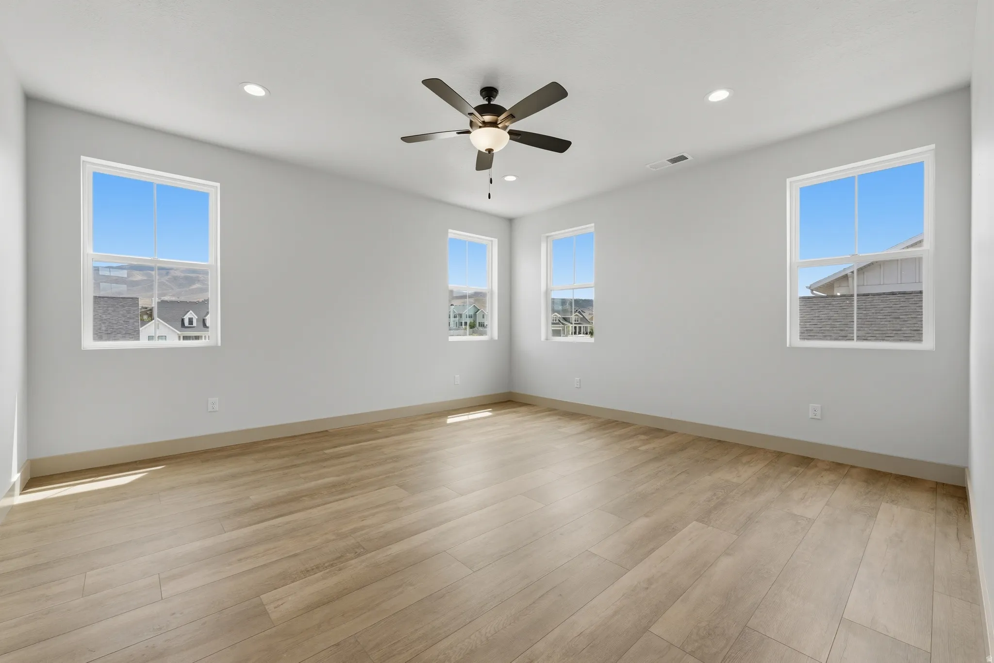 Primary Bedroom. Spacious room featuring wood-finish flooring, five windows, a ceiling fan with integrated lighting, and recessed ceiling lights