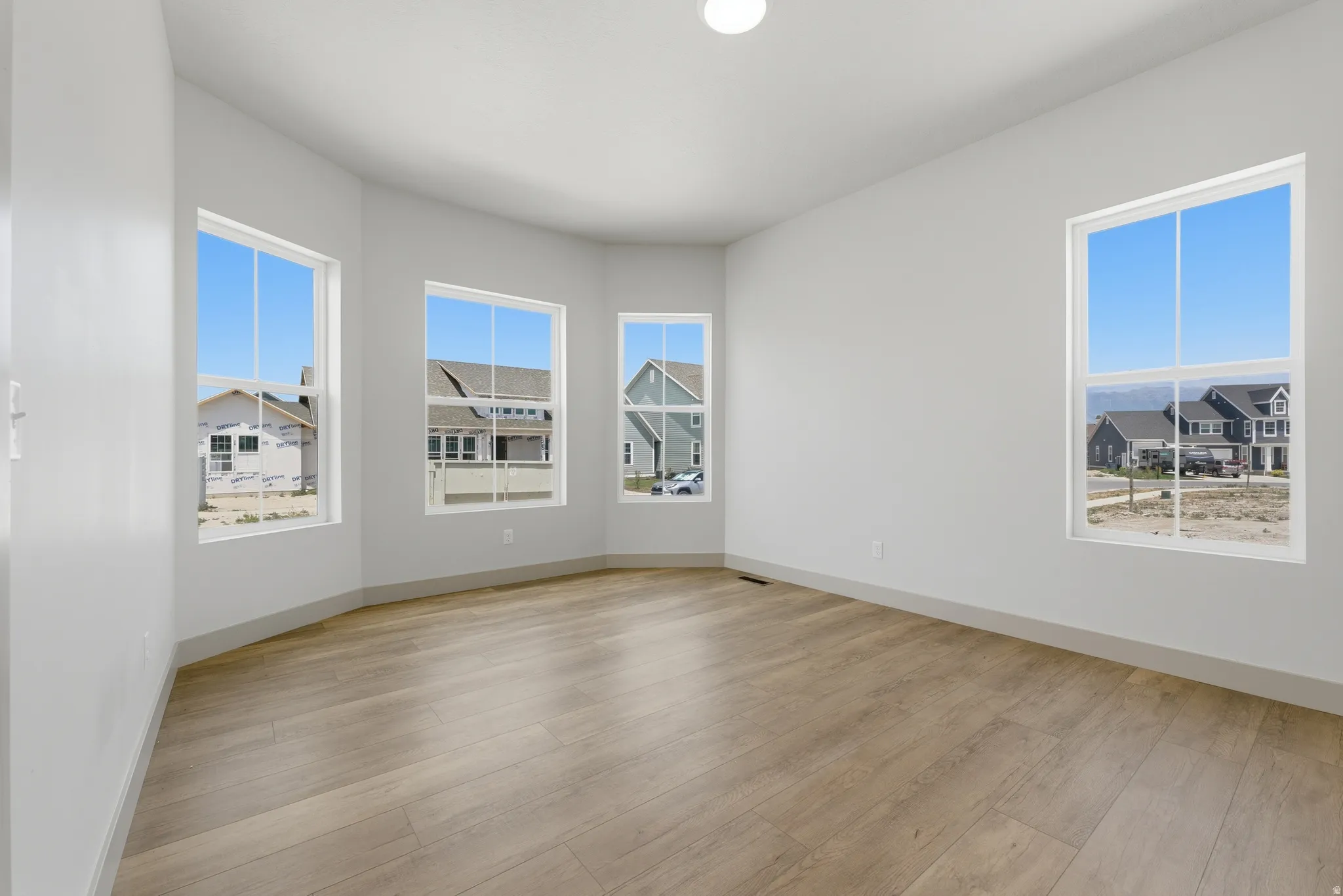 Bright interior space with wood-finish flooring, white walls, and multiple large windows