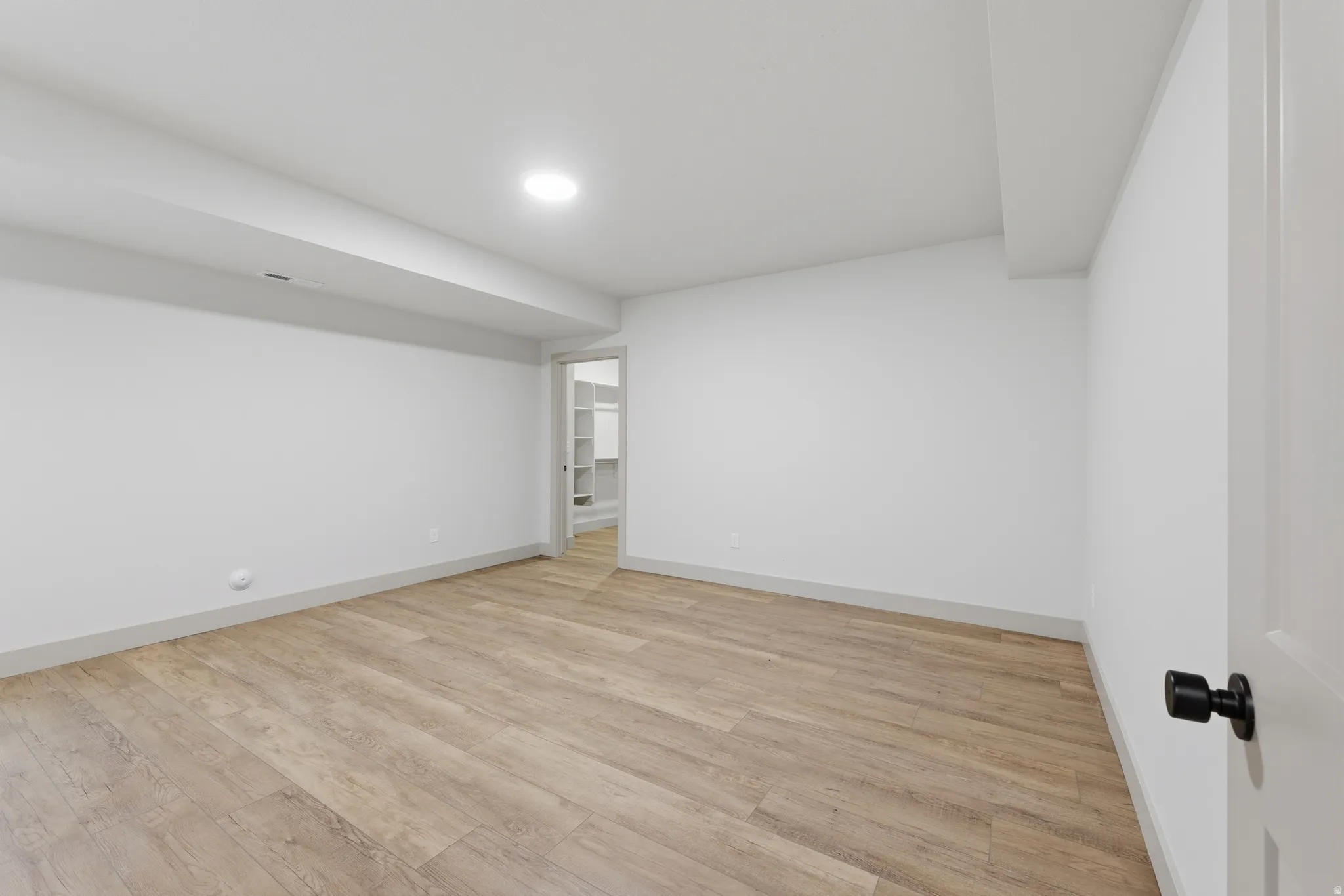 Spacious room featuring wood-finish flooring, white walls, recessed ceiling lighting, and a doorway leading to a walk-in closet with built-in shelving