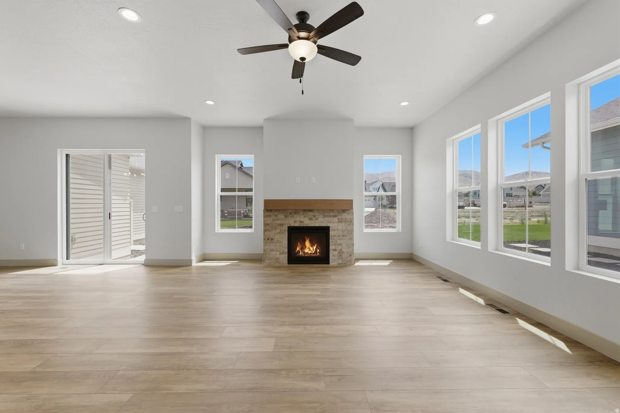 Spacious room with wood-finish flooring, a stone-clad fireplace with a wood mantle, and a ceiling fan