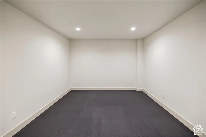 Neutral-toned interior space featuring recessed ceiling lighting, smooth walls, and dark flooring