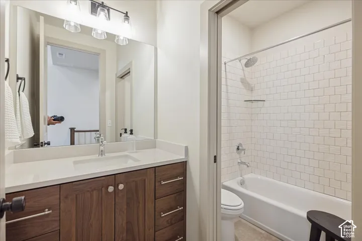 Bathroom featuring a dark wood-finish vanity with a white countertop and rectangular undermount sink, three-light wall fixture, large vanity mirror, and a tub-shower combination with white wall tile