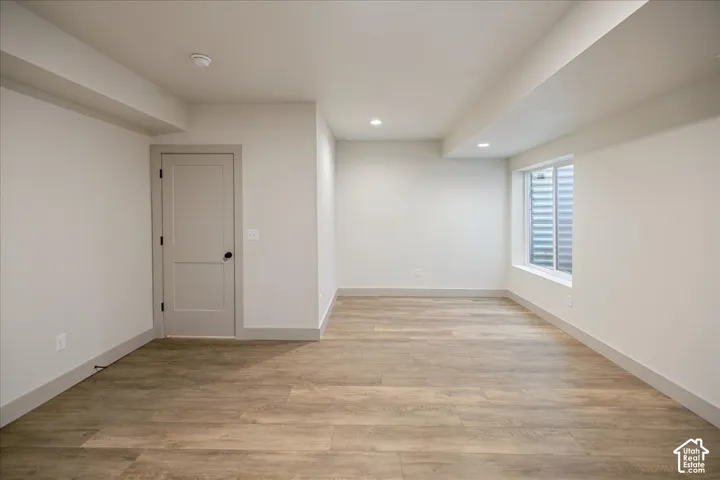 Neutral interior space featuring wood-finish flooring, recessed lighting, and a single-panel interior door with matte black hardware