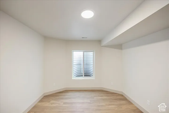 Room with wood-finish flooring, neutral walls, recessed ceiling lighting, and an egress window with a window well