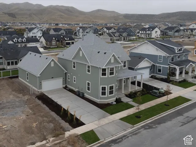 Two-story residence featuring light green siding, a pitched shingle roof, a front-facing attached garage with a concrete driveway, a covered front porch, and a mountain backdrop