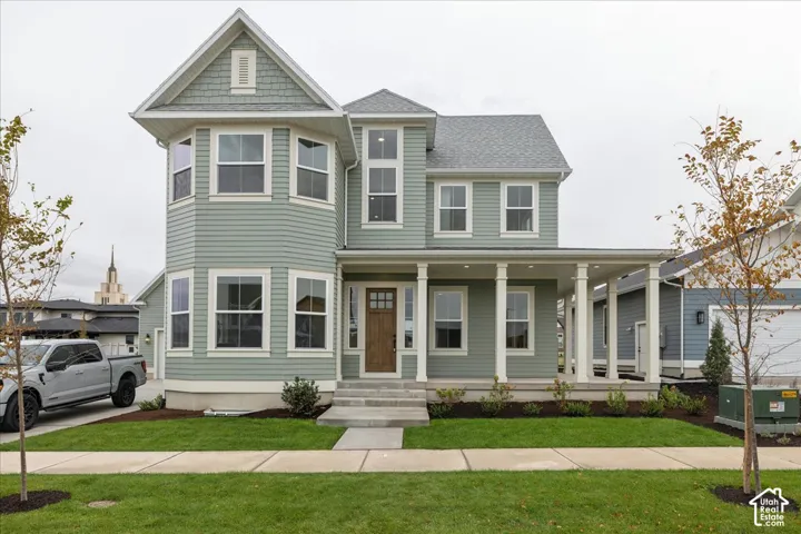 Two-story exterior featuring sage green horizontal lap siding, a wrap-around front porch with white columns, a natural wood entry door with multi-pane glass, and a combination of shingle and horizontal siding accents