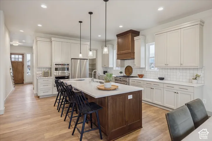 Kitchen featuring light-toned shaker cabinetry, a center island with a wood-finish base, stone countertops, square-tile backsplash, and a custom wood-paneled range hood