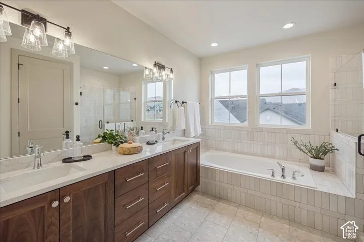 Primary SuiteDouble vanity with wood-finish cabinetry, quartz countertops, undermount sinks, deep soaking tub with vertical tile surround, and dual-light bar fixtures