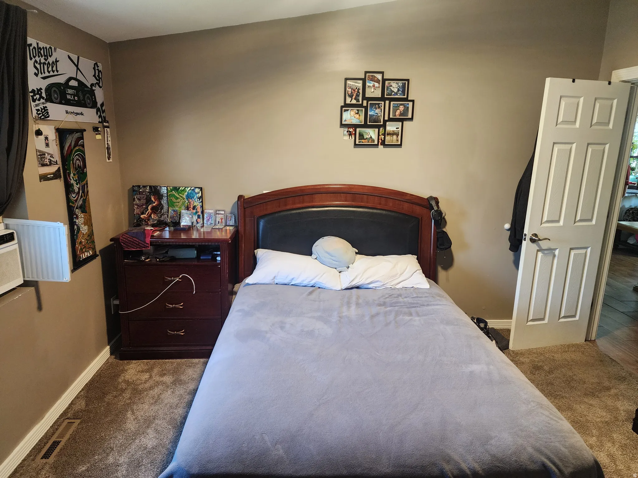Carpeted room featuring a wood-finish headboard with an integrated upholstered panel, a multi-paneled interior door, and a wall-mounted vent