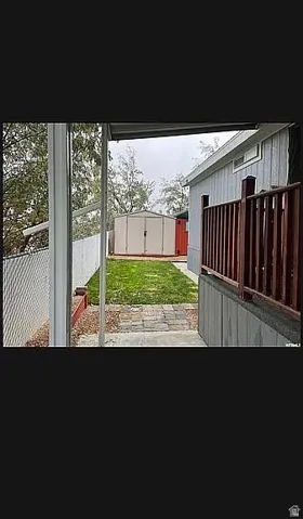 Fenced backyard featuring a paver pathway, manicured lawn, and a large storage shed