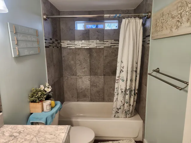Bathroom featuring a shower-tub combination with grey tile surround and decorative glass mosaic accent