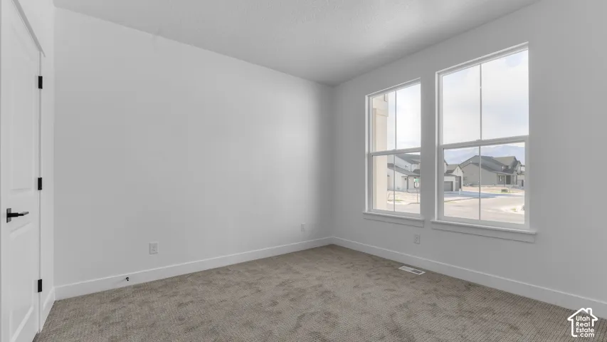 Neutral wall color, two large windows, carpeted flooring, white trim, and a white door with black hardware