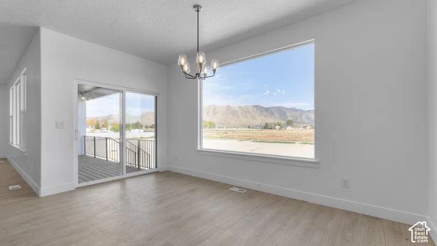 Spacious room with wood-finish flooring, a contemporary chandelier, large picture window, and sliding glass door leading to a covered deck