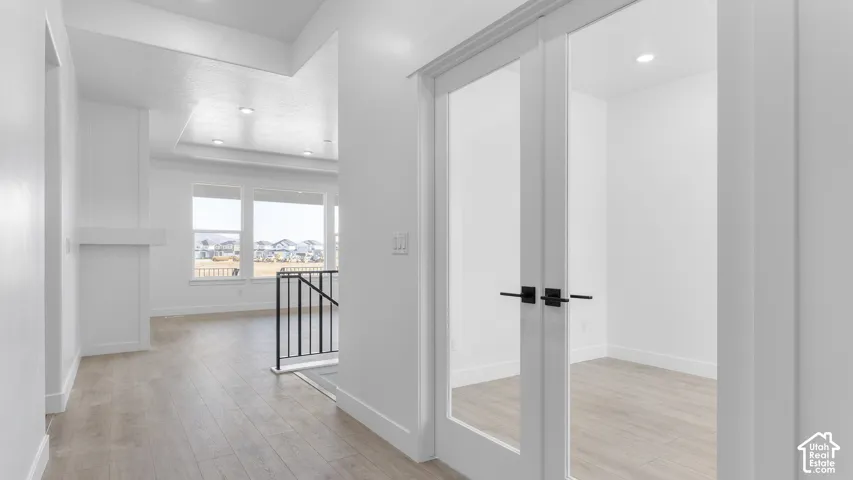 Light wood-finish flooring throughout, modern black railing, white walls, recessed ceiling lighting, and double glass-paneled doors with black hardware