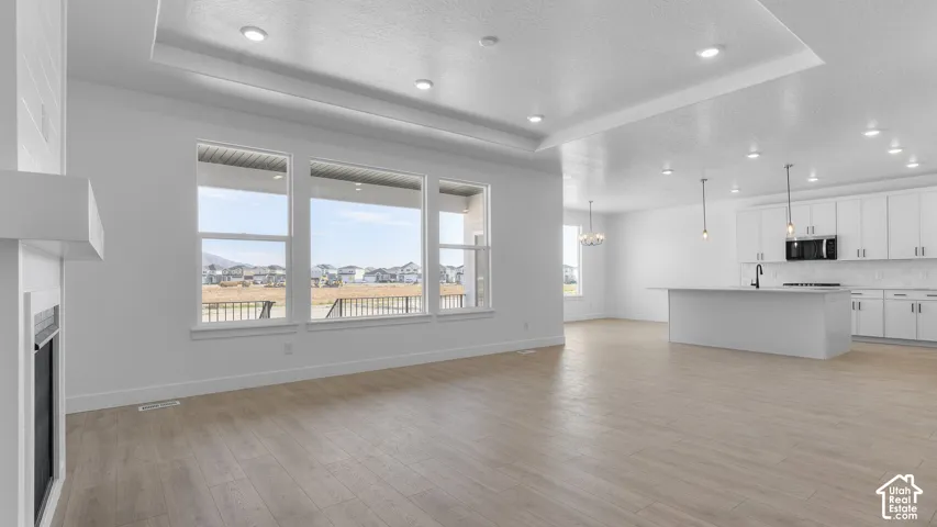 Open-concept living space with wood-finish flooring, a contemporary fireplace, and a kitchen featuring a large island, white cabinetry, and recessed lighting