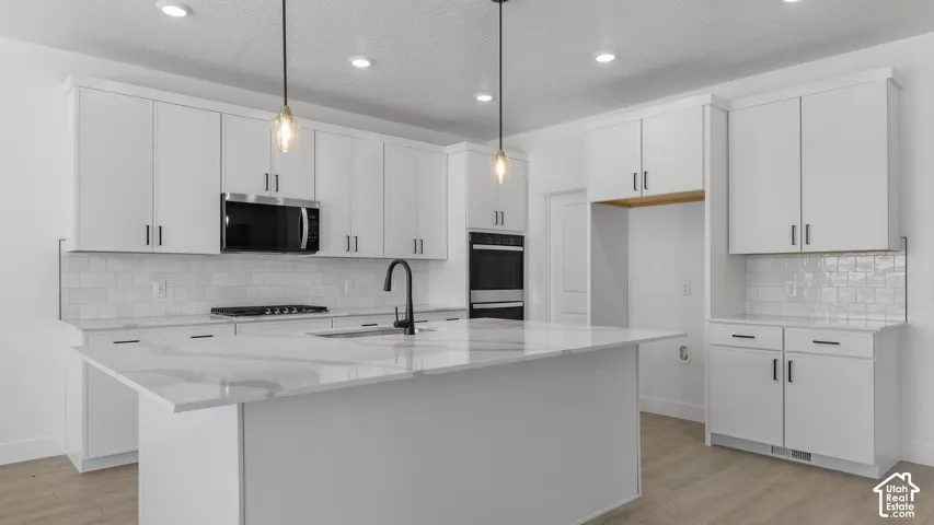White cabinetry with matte black hardware, large kitchen island with a white countertop, subway tile backsplash, and wood-finish flooring