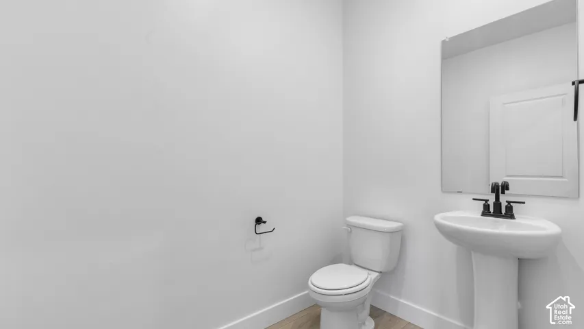 White pedestal sink with a matte black faucet, a framed mirror, and wood-finish flooring