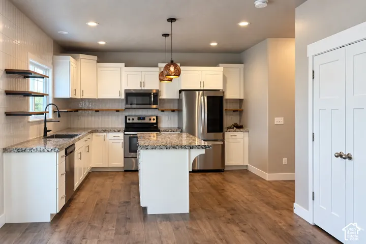 Open-concept kitchen featuring white cabinetry, granite countertops, stainless steel appliances, wood-finish flooring, and pendant lighting