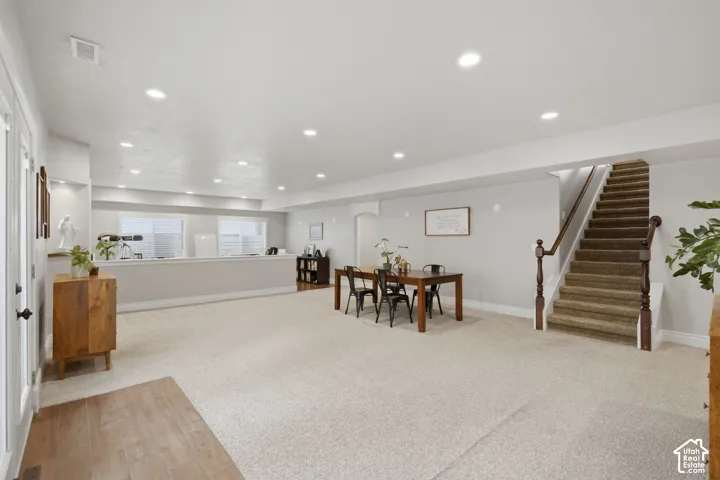 Spacious open area featuring recessed lighting, a neutral carpeted floor, a staircase with wood banister, and a half-wall with windows