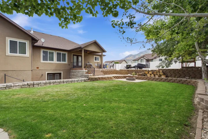Tiered backyard featuring a covered patio, stone retaining walls, a stone fire pit area, and a manicured lawn