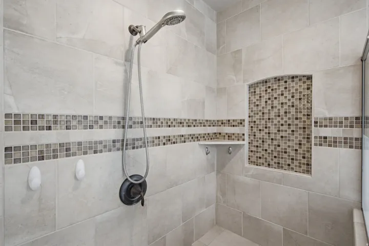 Tiled shower with a mosaic tile accent band, recessed niche with mosaic tile, and built-in corner shelf