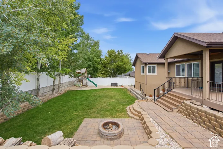 Expansive backyard featuring a paver patio with built-in fire pit, tiered landscaping with retaining walls, and a multi-level deck with stairs