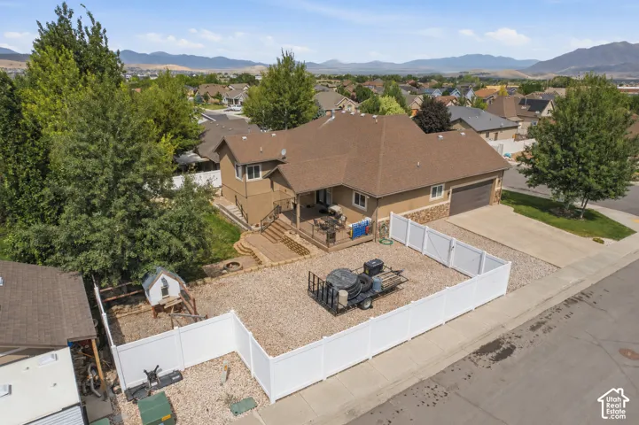 Two-story residence featuring a two-car garage, partial stone facade, and a deck with stairs descending to a tiered hardscape patio