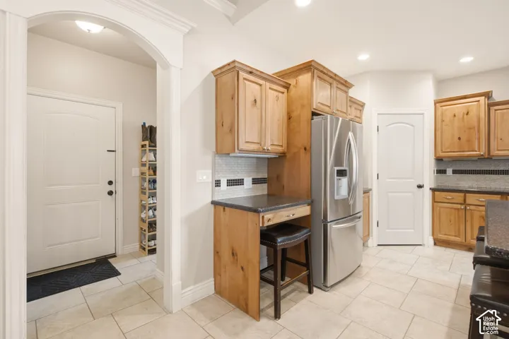 Kitchen featuring wood cabinetry, stainless steel refrigerator, dark countertops, and tile flooring