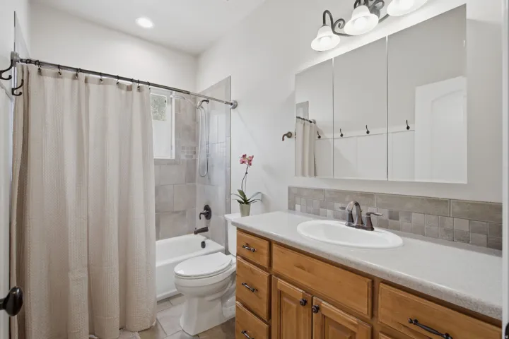 Bathroom featuring a wood-finish vanity with a light-toned countertop, an oval undermount sink with a bronze-tone faucet, a tiled backsplash, and a three-panel mirrored medicine cabinet