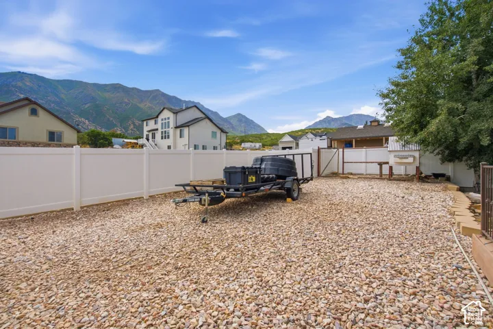 Expansive gravel yard featuring a white privacy fence, mature trees, mountain scenery, and a rear gate