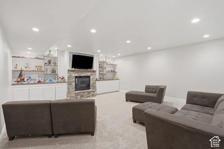 Spacious living area featuring a stacked stone fireplace with a mantle, recessed lighting, and built-in white cabinetry with wood-finish shelving
