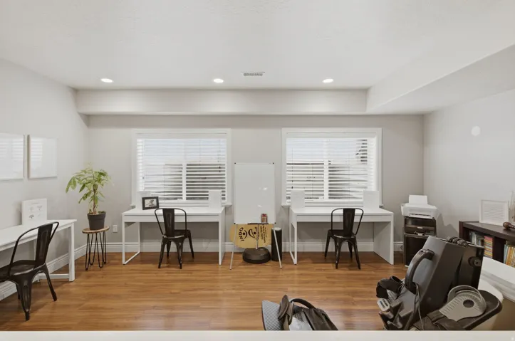 Spacious room featuring wood-finish flooring, two windows with blinds, recessed lighting, and light-toned wall finishes