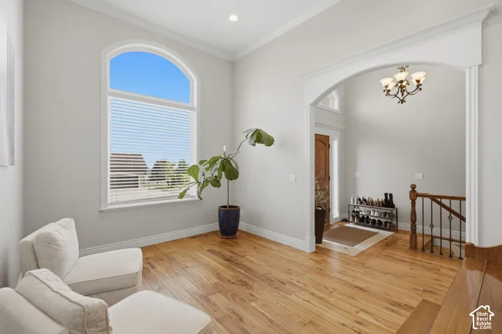 Living area featuring a large arched window with blinds, wood-finish flooring, and crown molding
