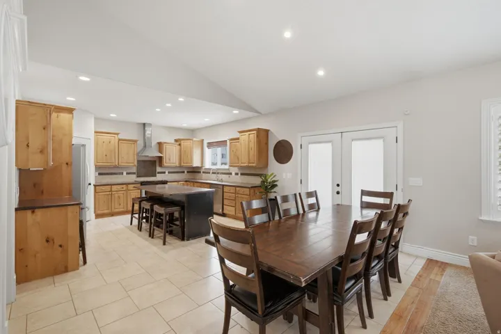 Spacious kitchen and dining area featuring light wood cabinetry, stone countertops, and a full tile backsplash