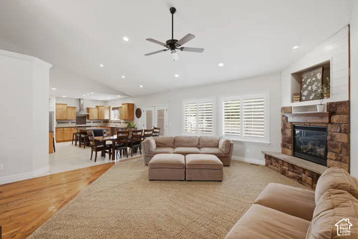 Spacious living area featuring a stone fireplace with shiplap accents, vaulted ceilings with recessed lighting, and a ceiling fan