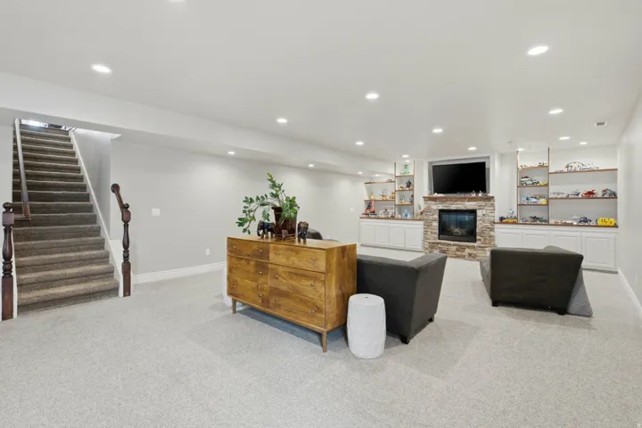 Spacious recreation room featuring light gray carpeting, a stone-clad fireplace with hearth, and recessed lighting