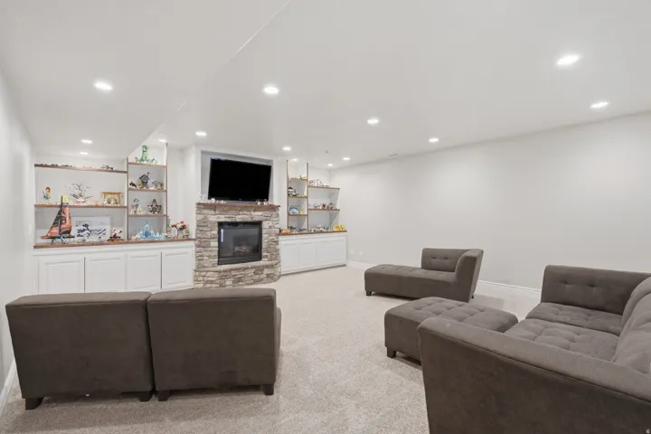 Spacious living area featuring a stacked stone fireplace with a mantle, recessed lighting, and built-in white cabinetry with wood-finish shelving