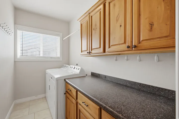 Functional utility space featuring light wood cabinetry, a speckled dark countertop, and a window for natural light