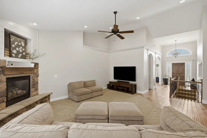 Spacious living area featuring a stone-clad fireplace with a hearth, a recessed wall niche with shiplap detailing, a ceiling fan, and recessed lighting
