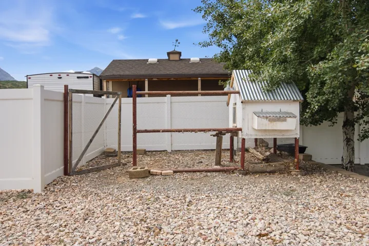 White privacy fencing enclosing a gravel area with a chicken coop featuring a corrugated metal roof