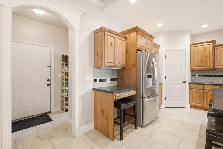Kitchen featuring wood cabinetry, stainless steel refrigerator, dark countertops, and tile flooring