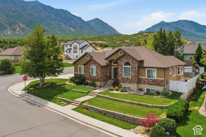 Mountain backdrop frames this residence featuring a stone and stucco exterior, arched window, tiered landscaping, paved walkways, and a side yard with white fencing