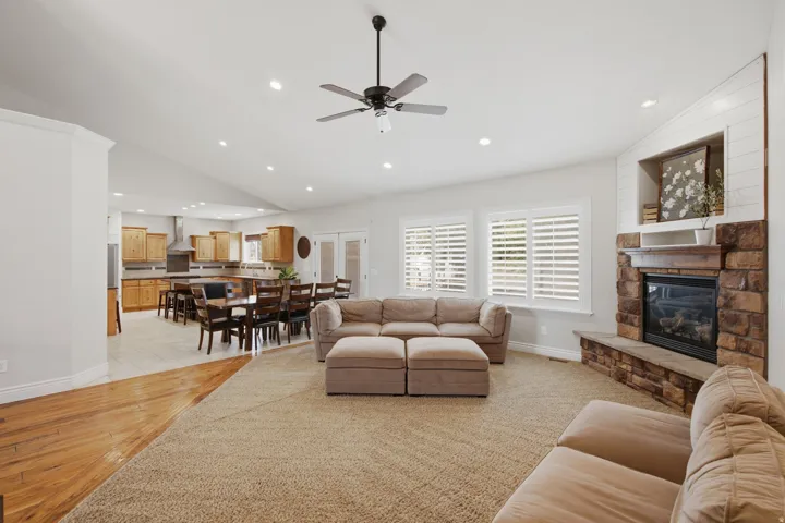 Spacious living area featuring a stone fireplace with shiplap accents, vaulted ceilings with recessed lighting, and a ceiling fan
