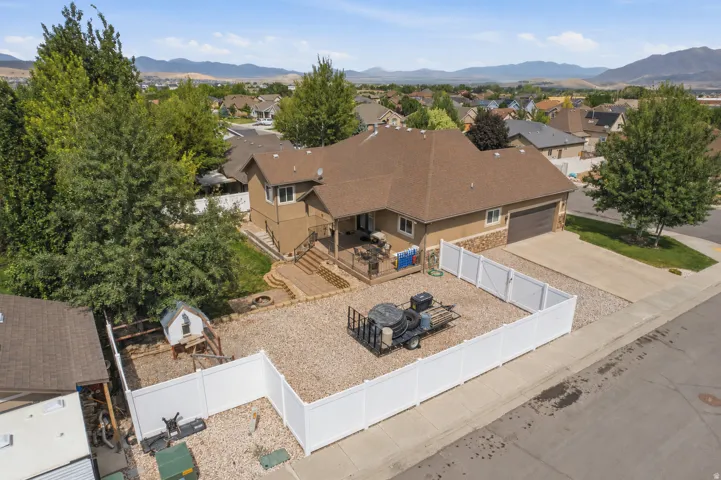 Two-story residence featuring a two-car garage, partial stone facade, and a deck with stairs descending to a tiered hardscape patio