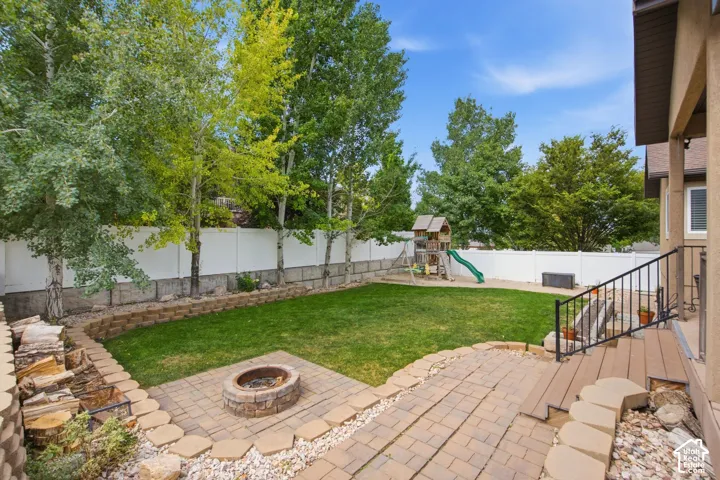 Expansive backyard featuring a lush lawn, a stone fire pit area, and a large paver patio with steps leading to the home's exterior